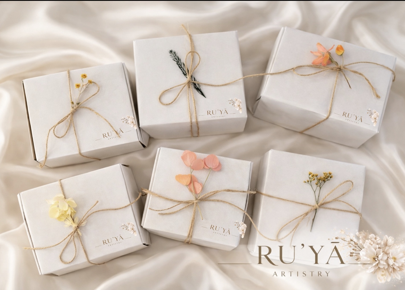 A collection of six Ru'yā Artistry gift boxes on cream silk &mdash; each tied with jute and a dried bloom